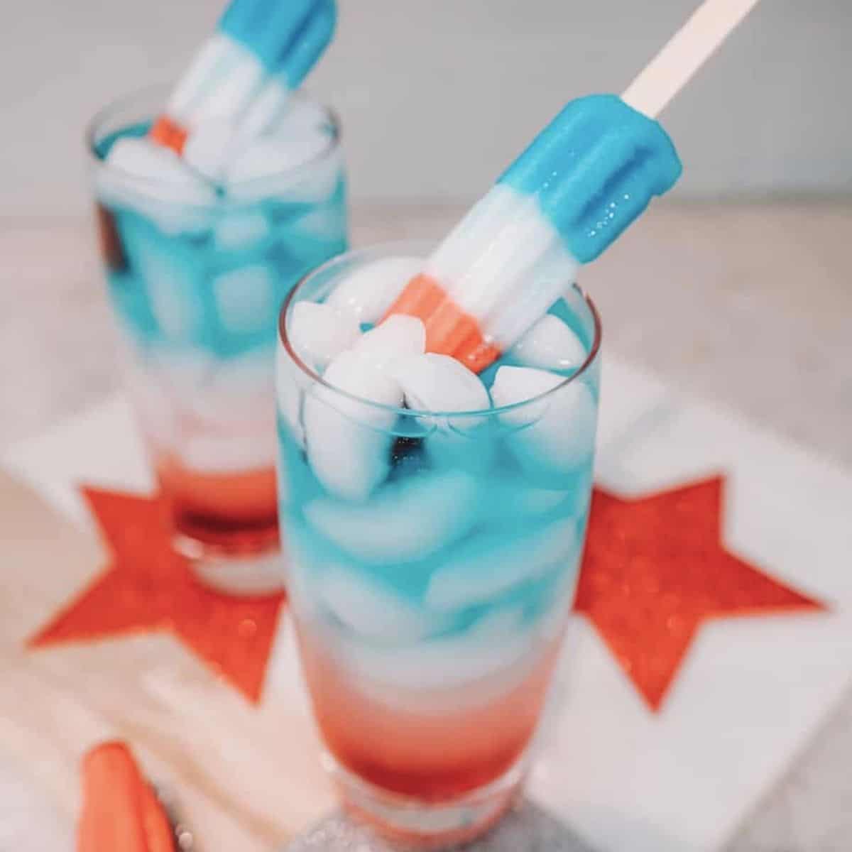 Red white and blue cocktail topped with a popsicle. 