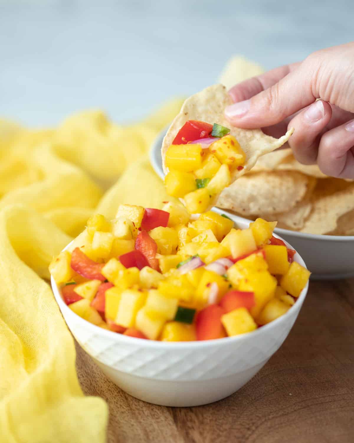 Hand dipping a chip into the pineapple mango salsa.
