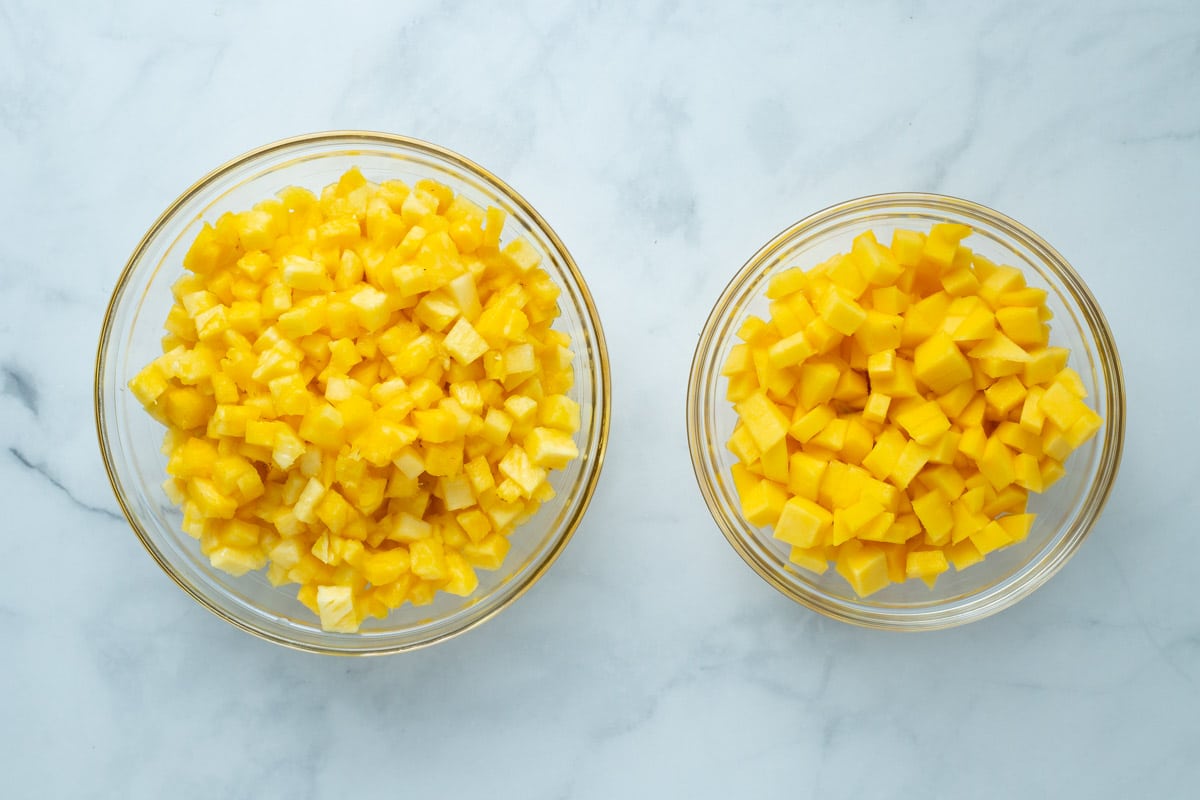 Pineapple chunks, and mango chunks in two glass bowls.
