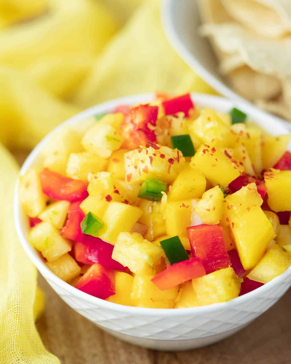 Pineapple mango salsa topped with red pepper flakes in a small white serving bowl.
