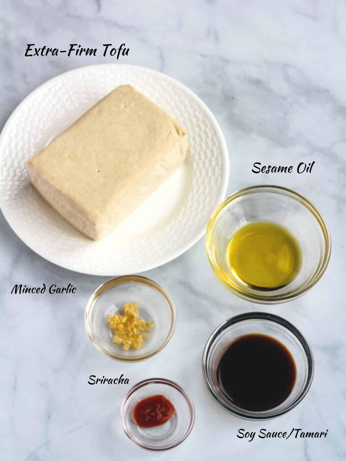 Spicy air fryer tofu ingredients: extra firm tofu block, sesame oil, soy sauce, sriracha, and minced garlic.
