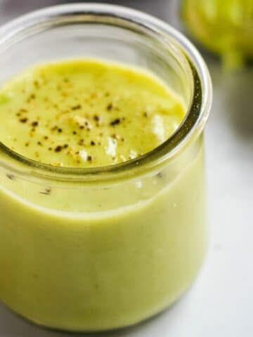 Vegan avocado dressing topped with black pepper in a glass jar.