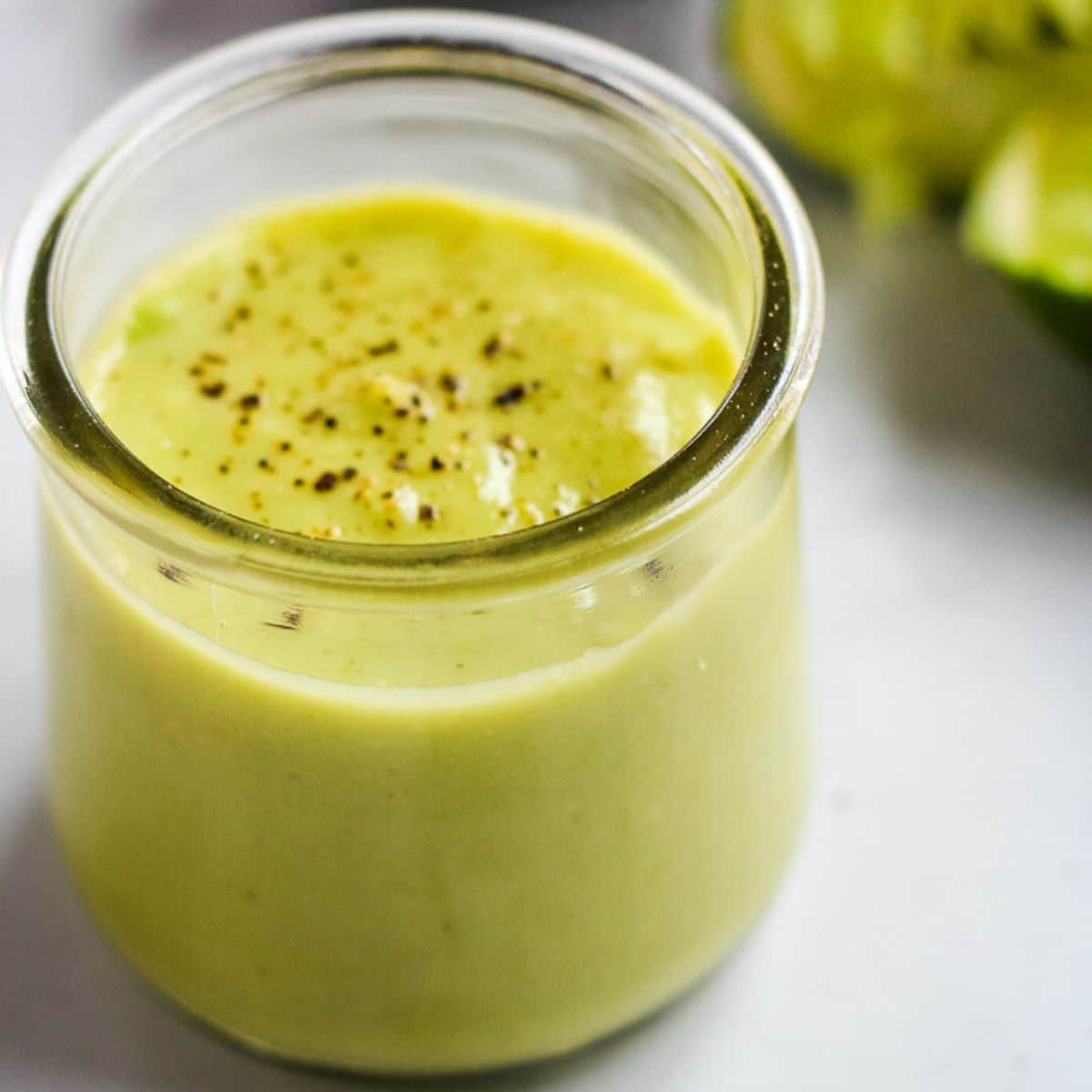 Vegan avocado dressing topped with black pepper in a glass jar.