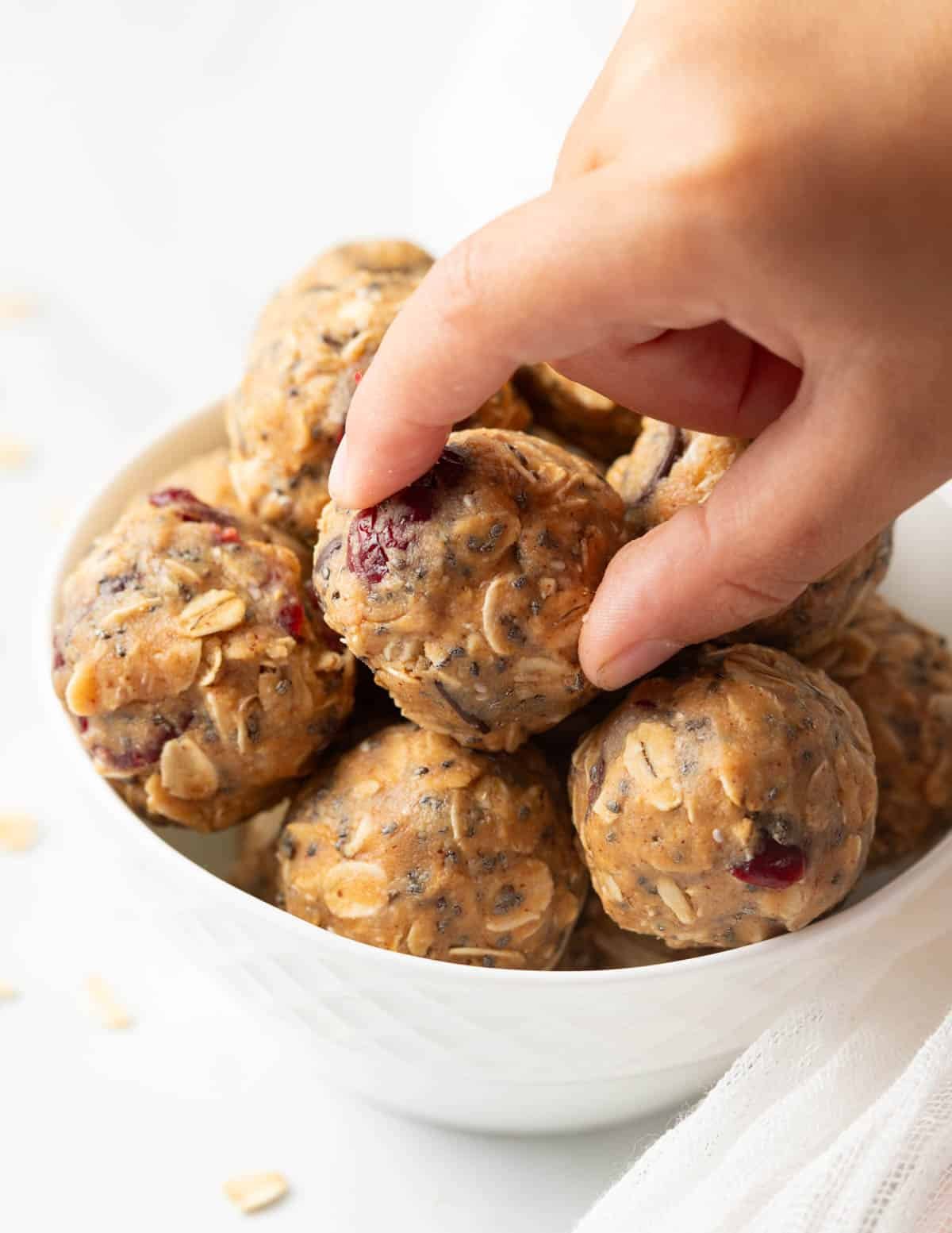 Hand reaching for an almond butter protein ball in a bowl.