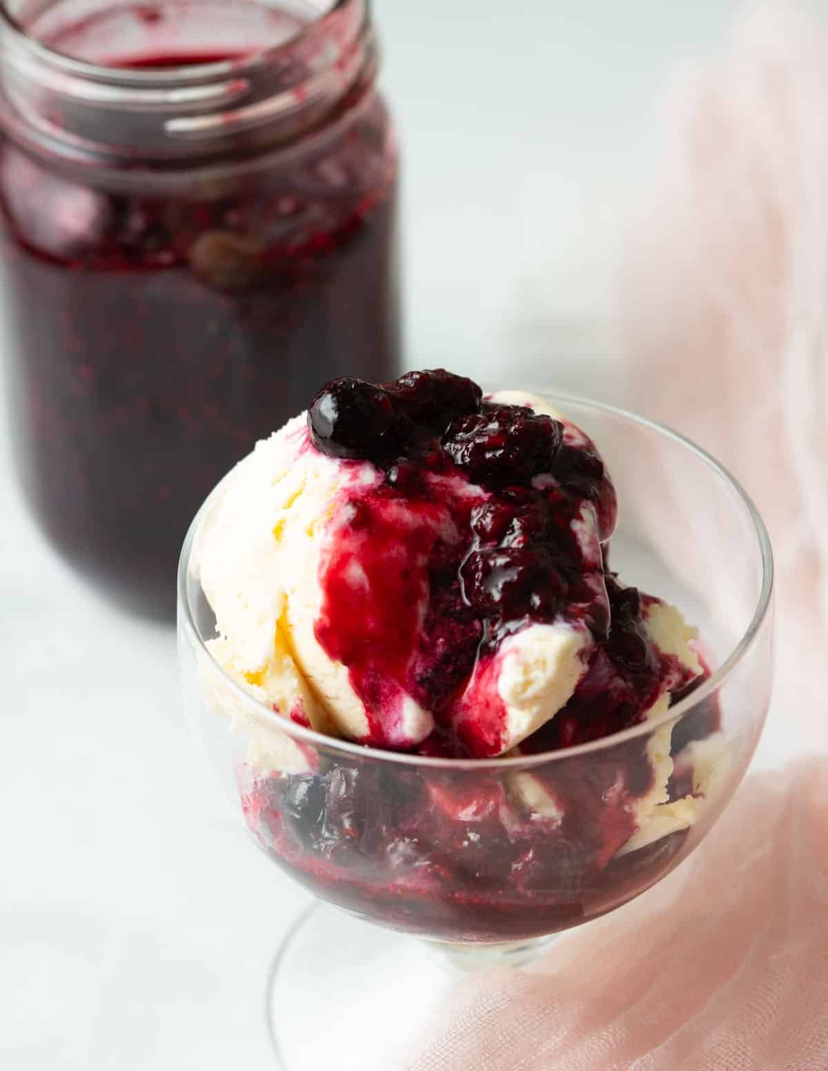 Berry compote in a jar beside vanilla ice cream topped with berry compote.
