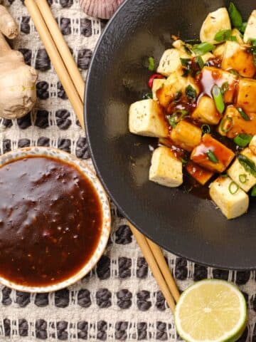 Korean BBQ sauce in small bowl beside tofu bowl topped with sauce.