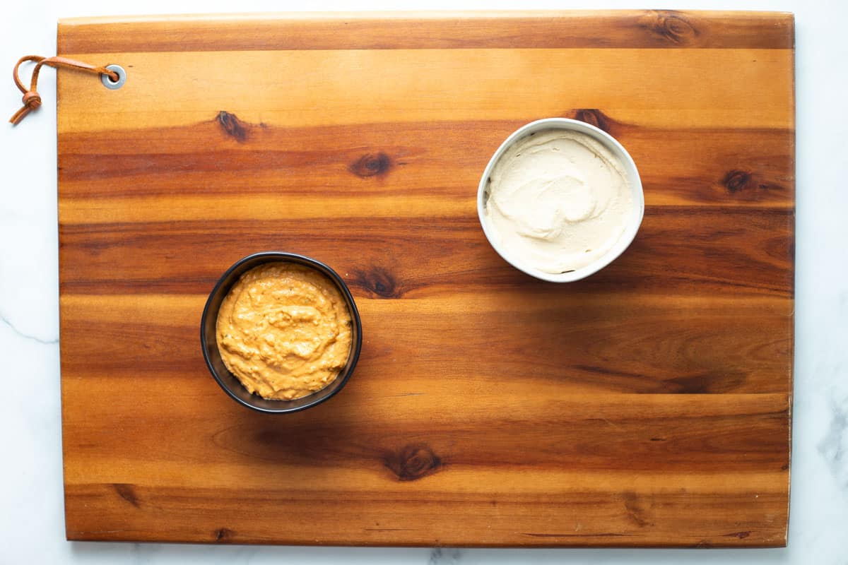 Two dips in small bowls on a wood serving tray.

