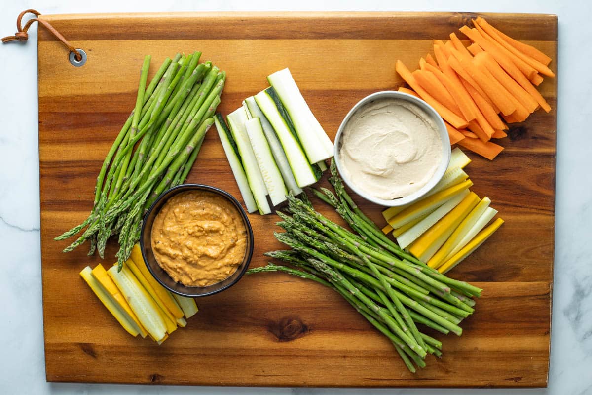 Two dips with asparagus, zucchini, yellow squash, and carrots on a serving tray.
