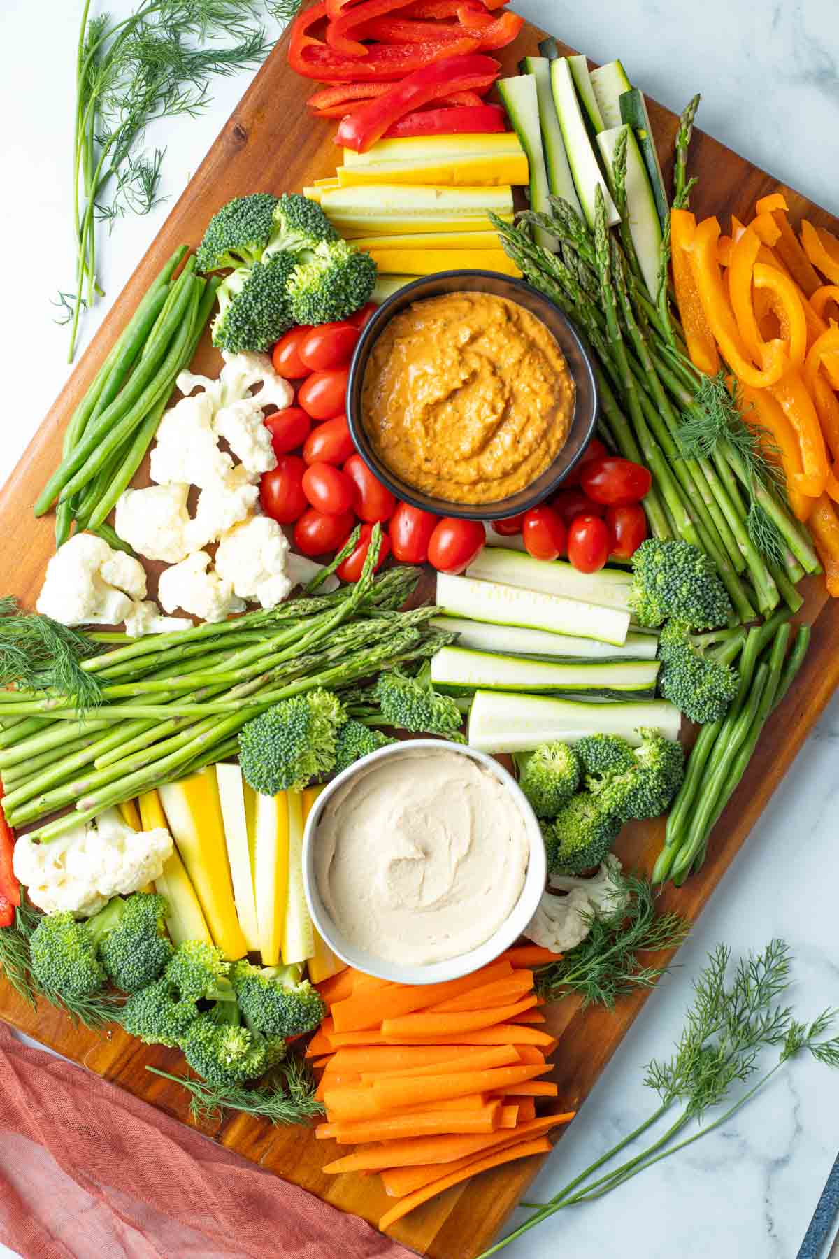 Overhead of a large vegetable tray with colorful vegetables and two types of dips.
