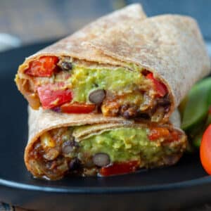 Black bean burrito cut in half and served on a black plate.
