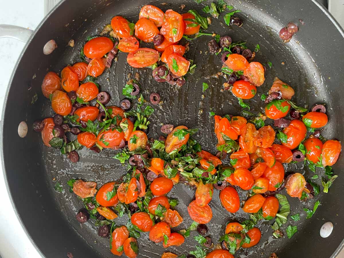Tomatoes, olives, and herbs in saute pan.
