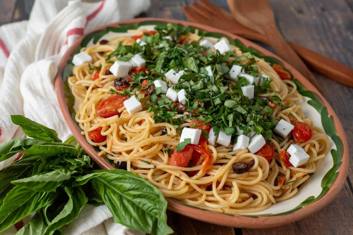 Greek spaghetti topped with fresh herbs and feta cheese cubes.

