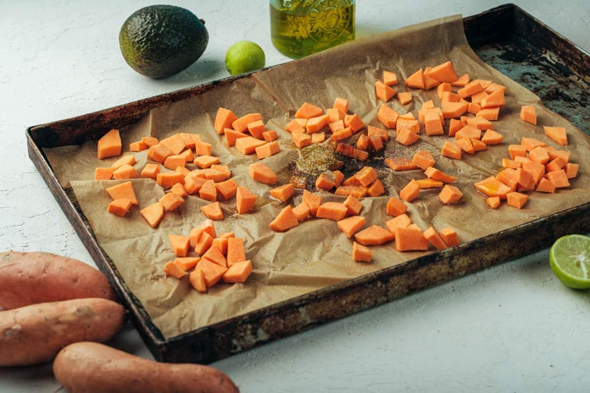 Spices and olive oil added to diced sweet potatoes on a baking sheet.