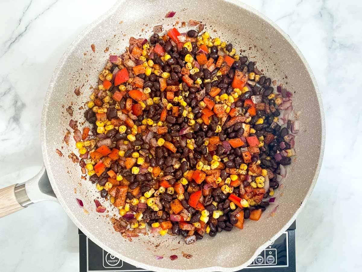 Vegan enchilada filling: black beans, peppers, corn, and onions in saute pan.