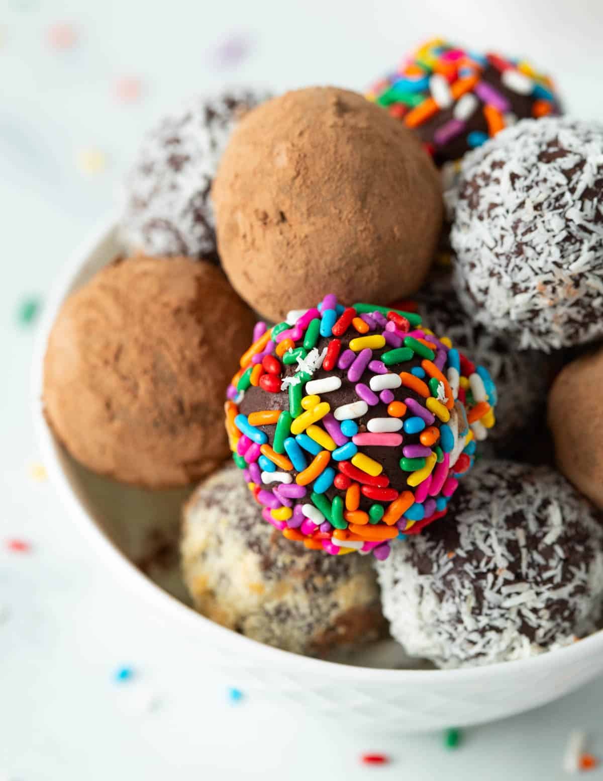Vegan chocolate truffles covered in assorted coatings: sprinkles, coconut, cocoa powder, and nuts.