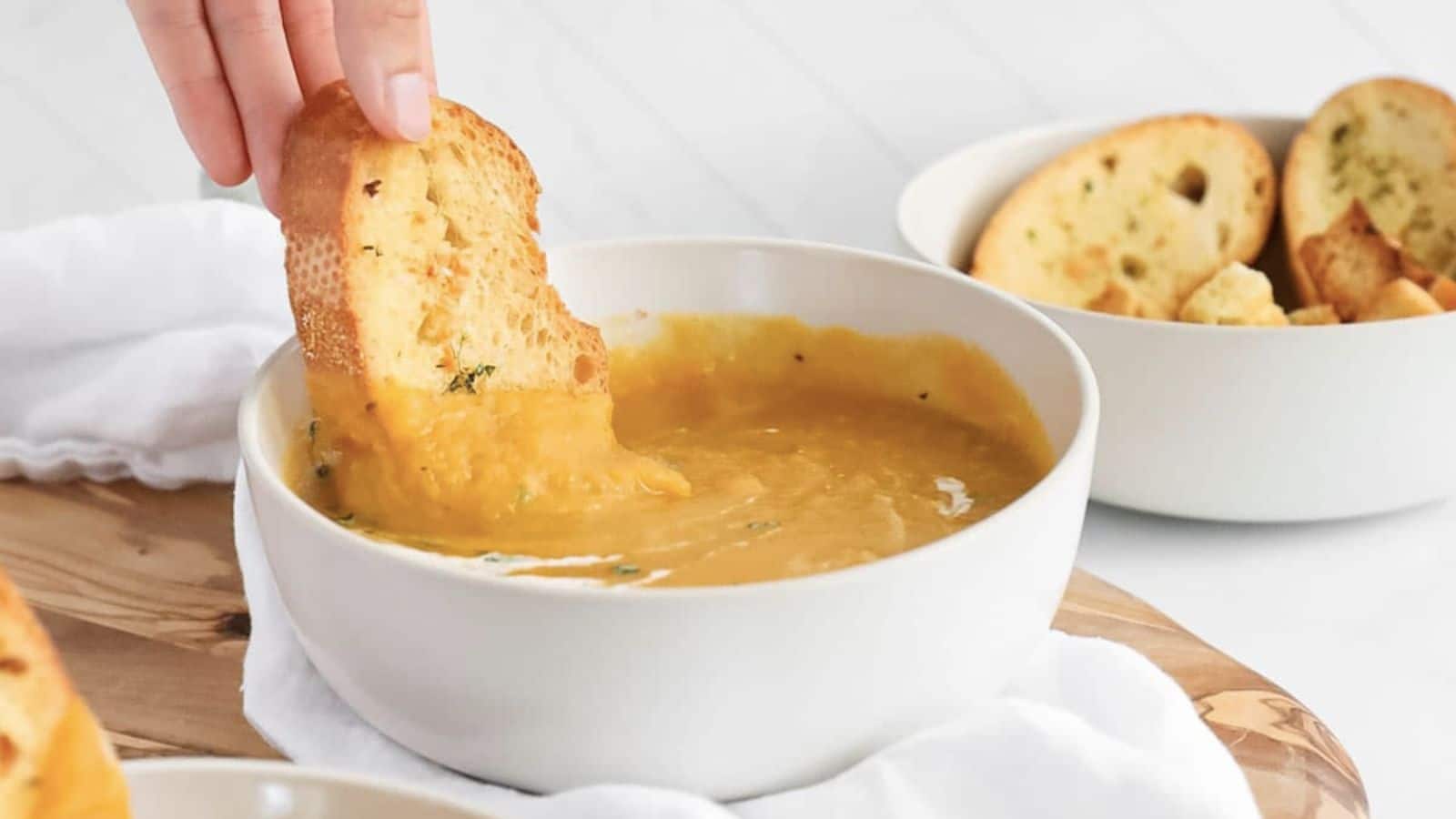 Hand dipping bread into bowl of butternut squash and apple soup. 
