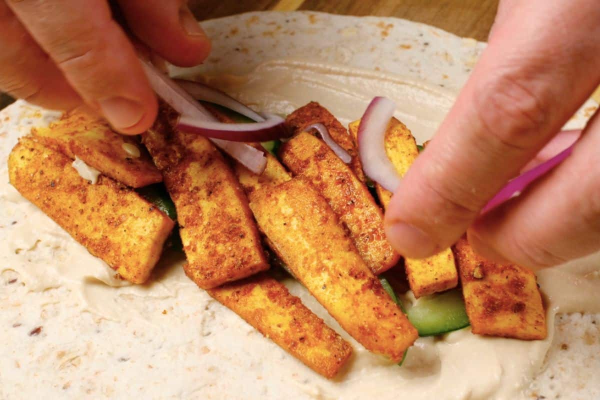 Adding tofu strips to pita bread with cucumbers, tomatoes, and onions. 
