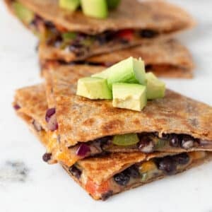 Vegan quesadillas with black beans and vegetables topped with sliced avocado.