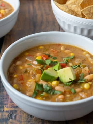 Bowl of vegan white bean chili topped with diced avocado and cilantro.