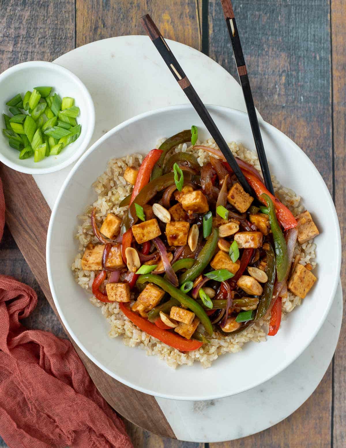 Vegan kung pao tofu in serving bowl with a side of green onions and chop sticks.