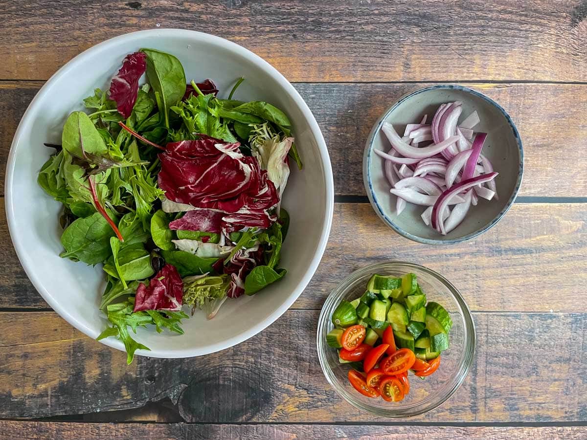 Mixed greens in large bowl, sliced red onion, and diced cucumber, and halved tomatoes.