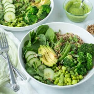 White bowls filled with green vegetables and quinoa topped with Green Goddess dressing.