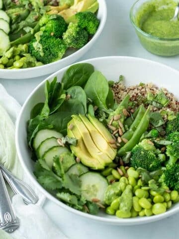 White bowls filled with green vegetables and quinoa topped with Green Goddess dressing.