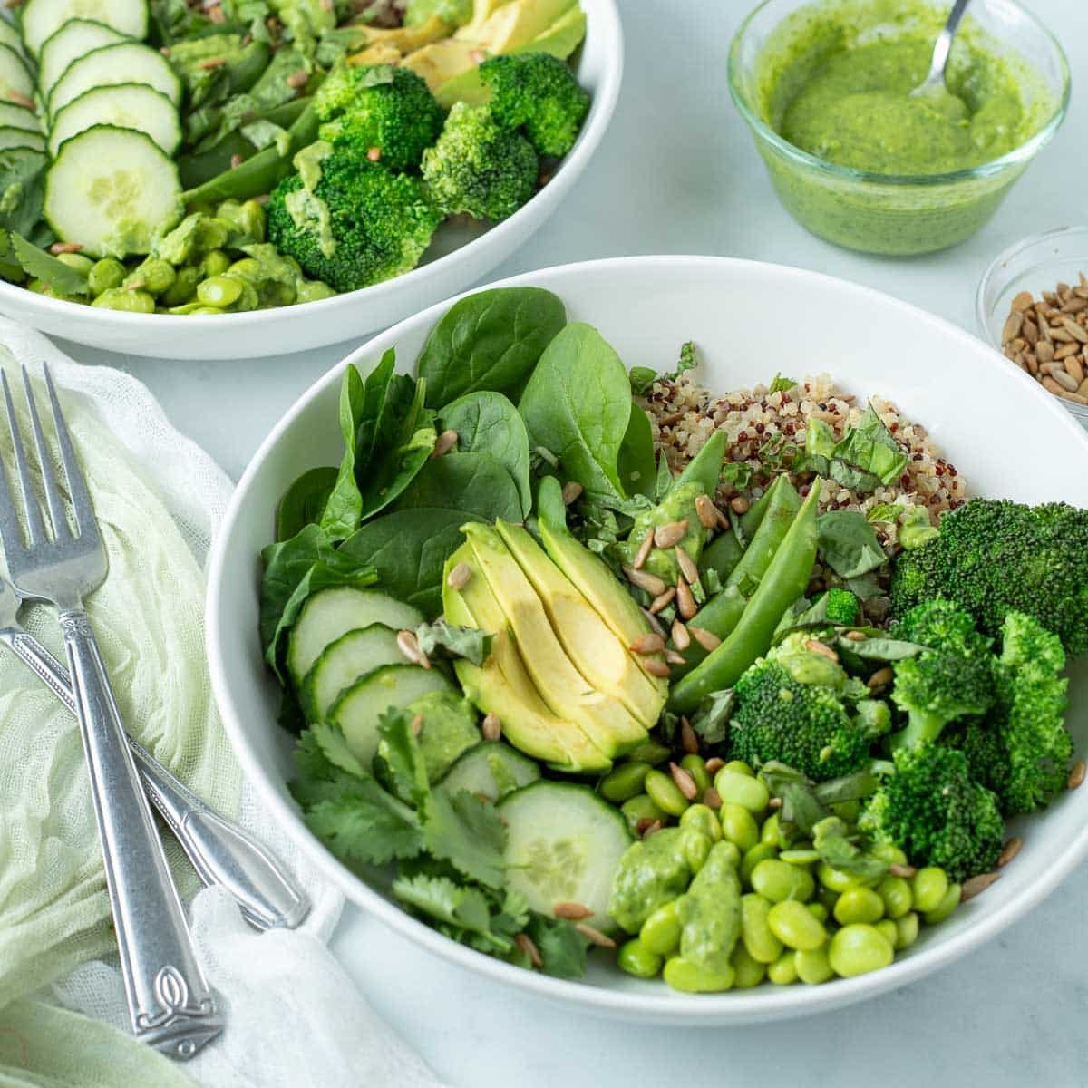 White bowls filled with green vegetables and quinoa topped with Green Goddess dressing