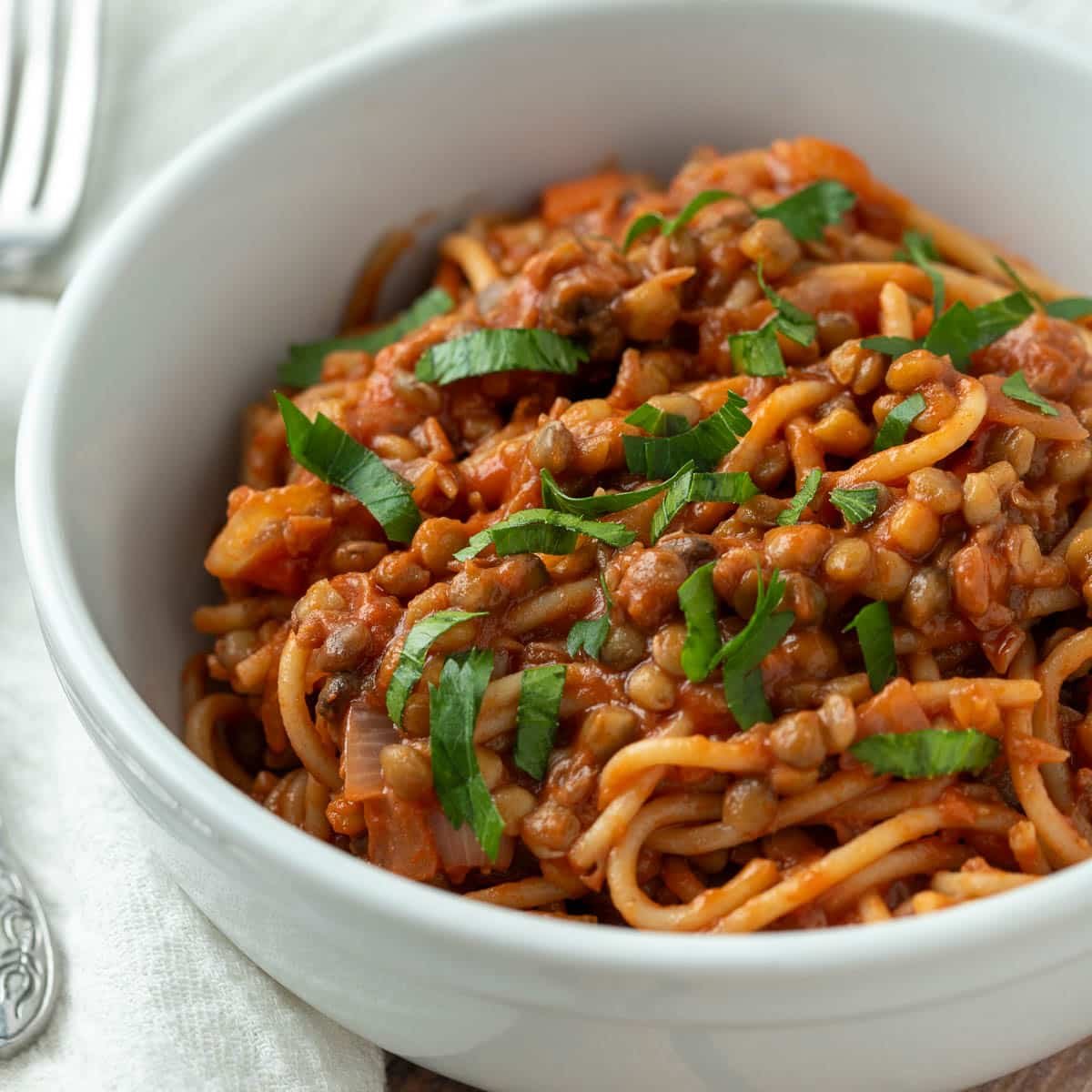 Vegan bolognese served with spaghetti and topped with chopped parsley.