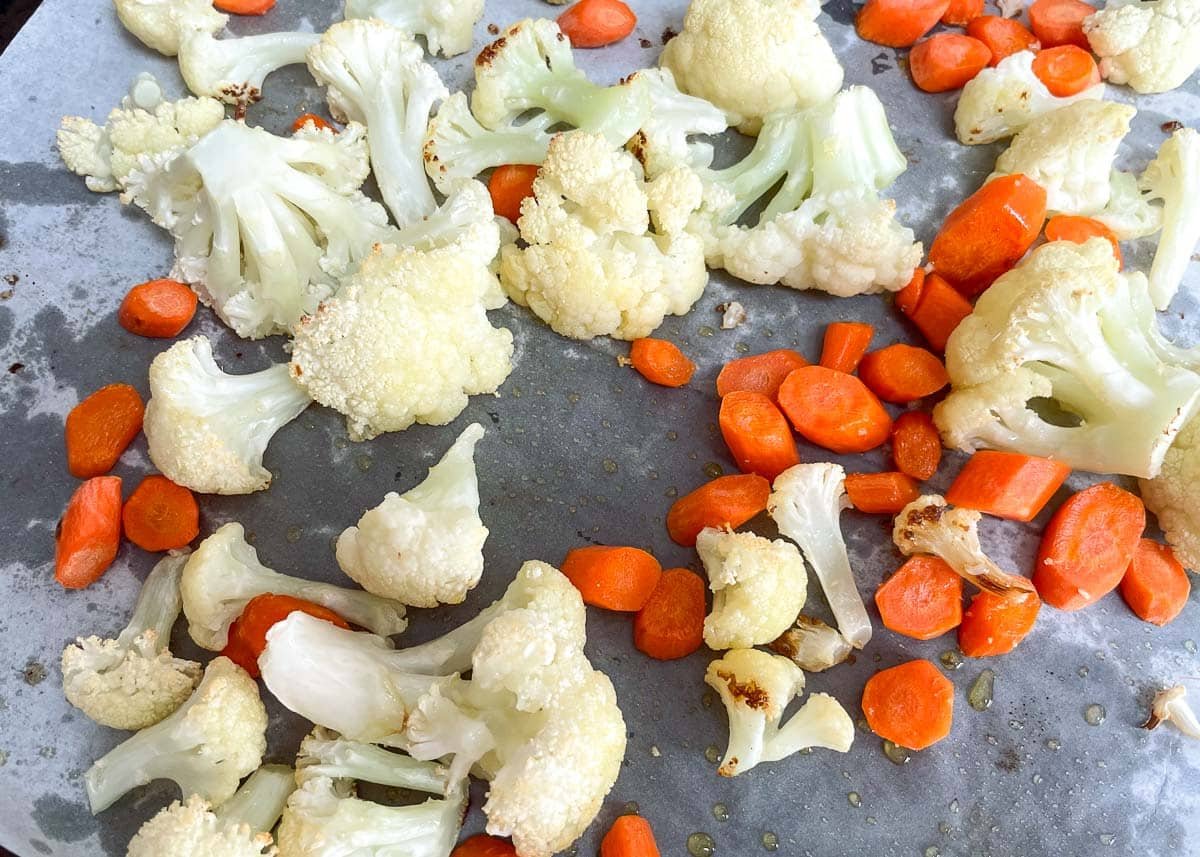 Roasted cauliflower and carrots on a baking sheet lined with parchment paper.