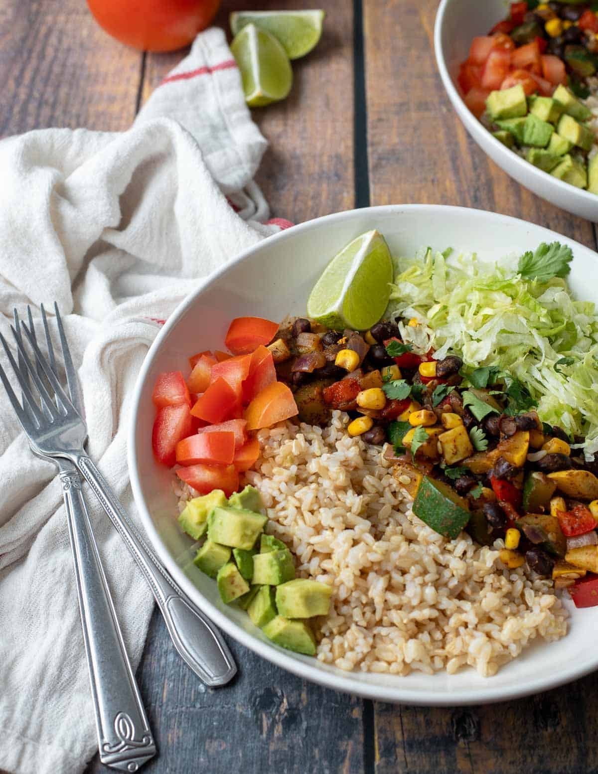 Vegan burrito bowl with brown rice, mixed vegetables, shredded lettuce, tomatoes, and avocados.