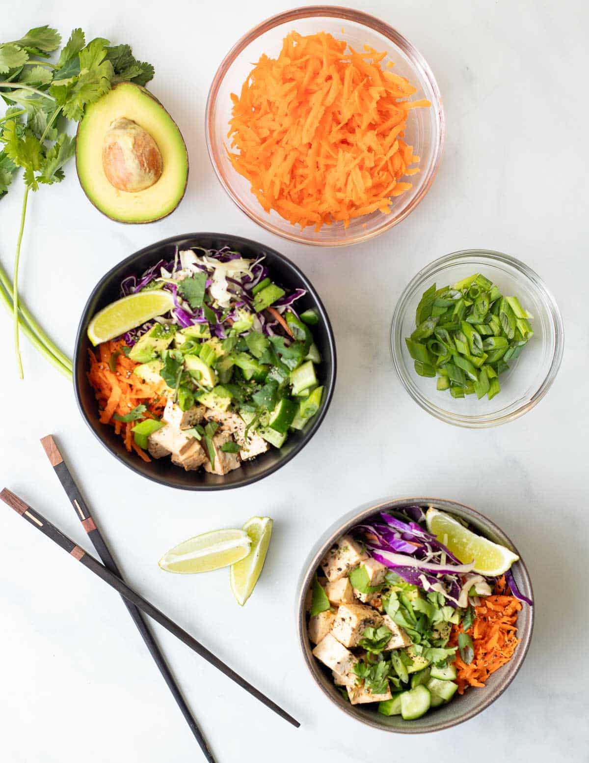 Two vegan poke bowls, overhead with shredded carrots, and chopped green onion.