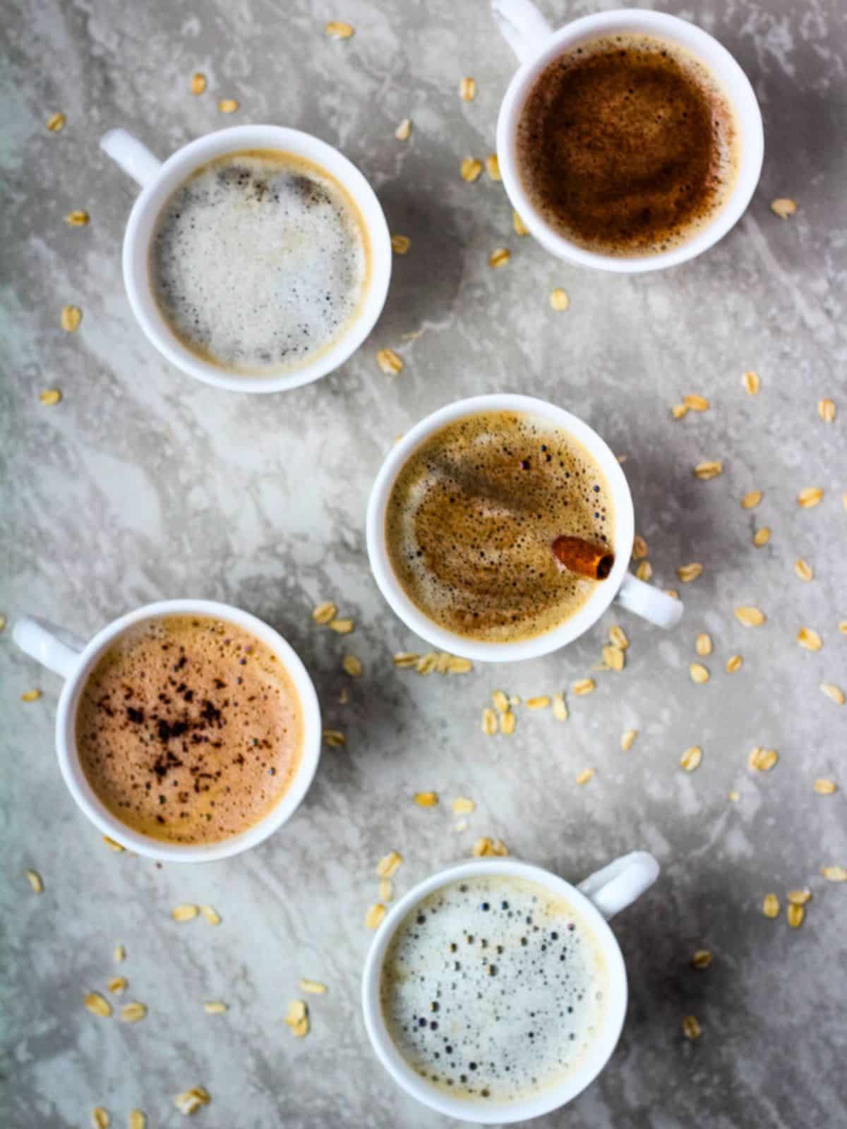Overhead of oat milk lattes in small white mugs.