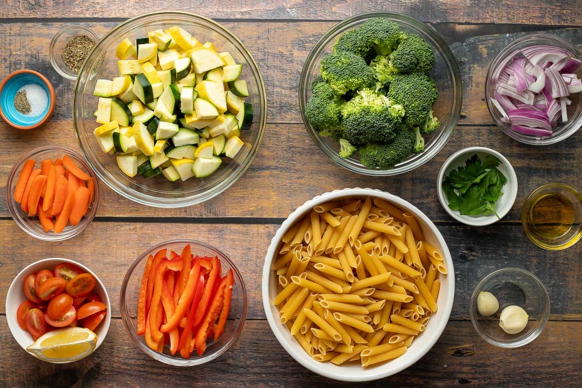 Salt, pepper, Italian seasoning, diced squash, carrots, cherry tomatoes, lemon wedge, red pepper slices, penne pasta, broccoli florets, red onion slices, parsley, olive oil, garlic cloves.