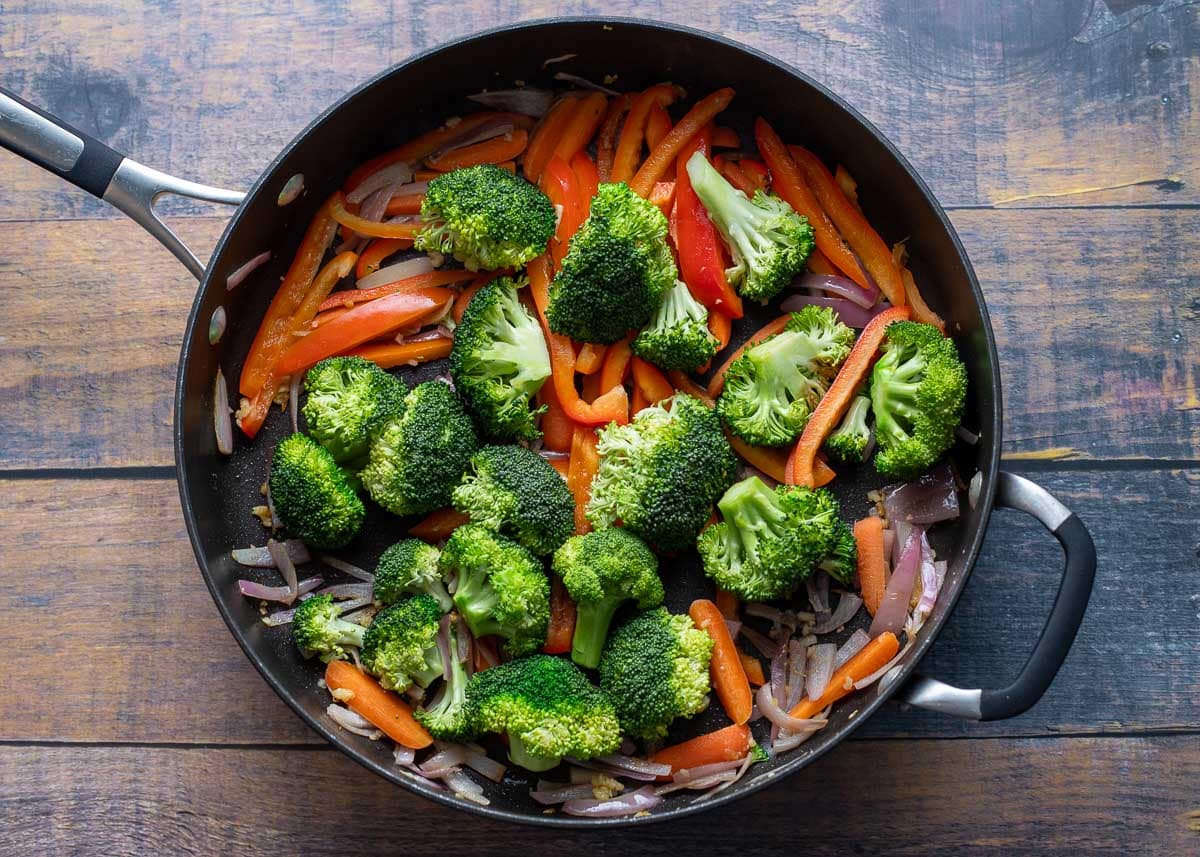 Broccoli and red peppers added to onions and carrots in saute pan.