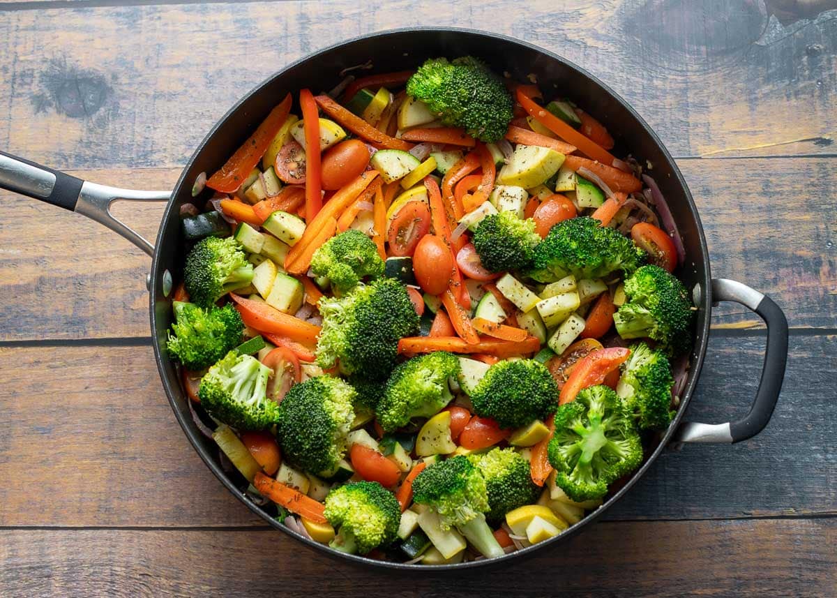 Tomatoes and herbs added to pan of vegetables.