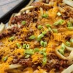 Loaded vegan dirty fries on a baking sheet covered with chili, cheese, and scallions.