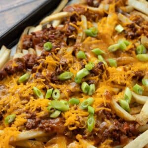 Loaded vegan dirty fries on a baking sheet covered with chili, cheese, and scallions.