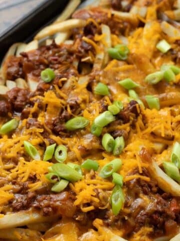 Loaded vegan dirty fries on a baking sheet covered with chili, cheese, and scallions.