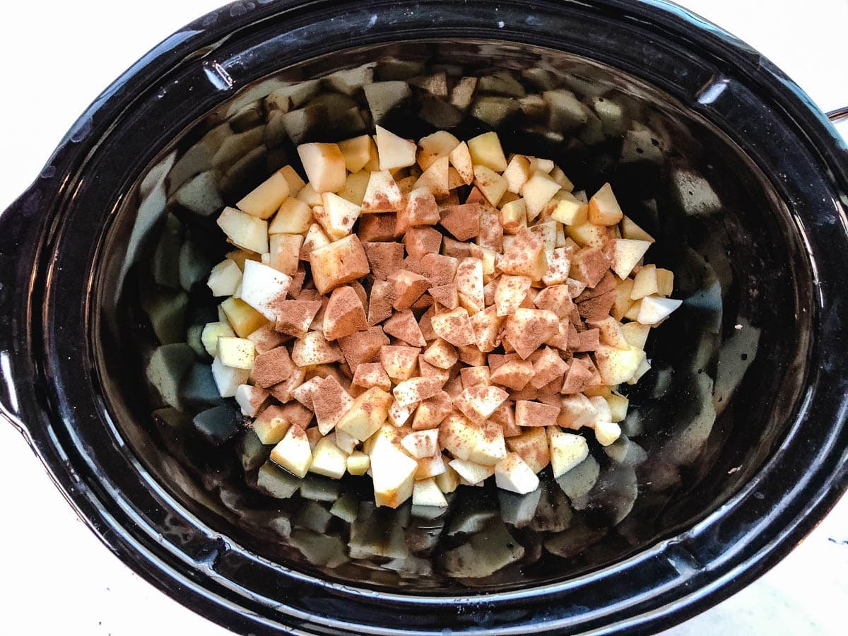 Diced apples topped with cinnamon in a black slow cooker.