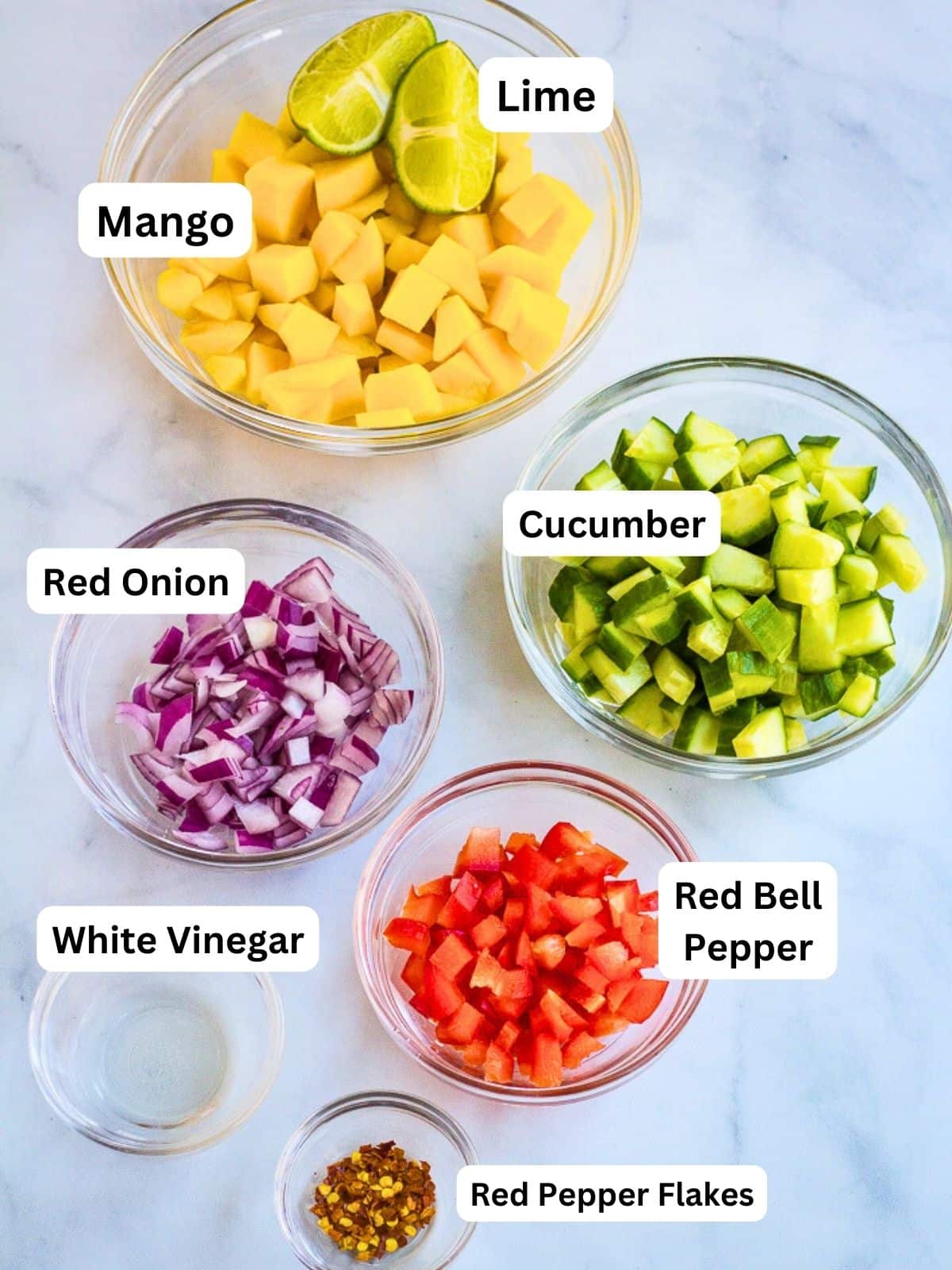 Mango salad ingredients: diced mango, lime, diced red onion, diced cucumber, diced red pepper, white vinegar, red pepper flakes.