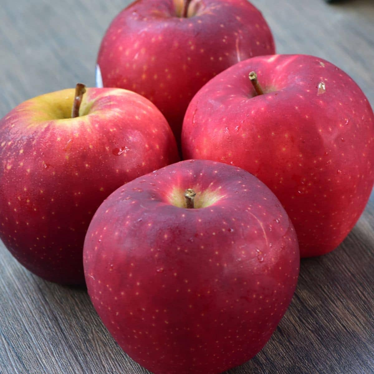 Four red queen apples on a wood table.