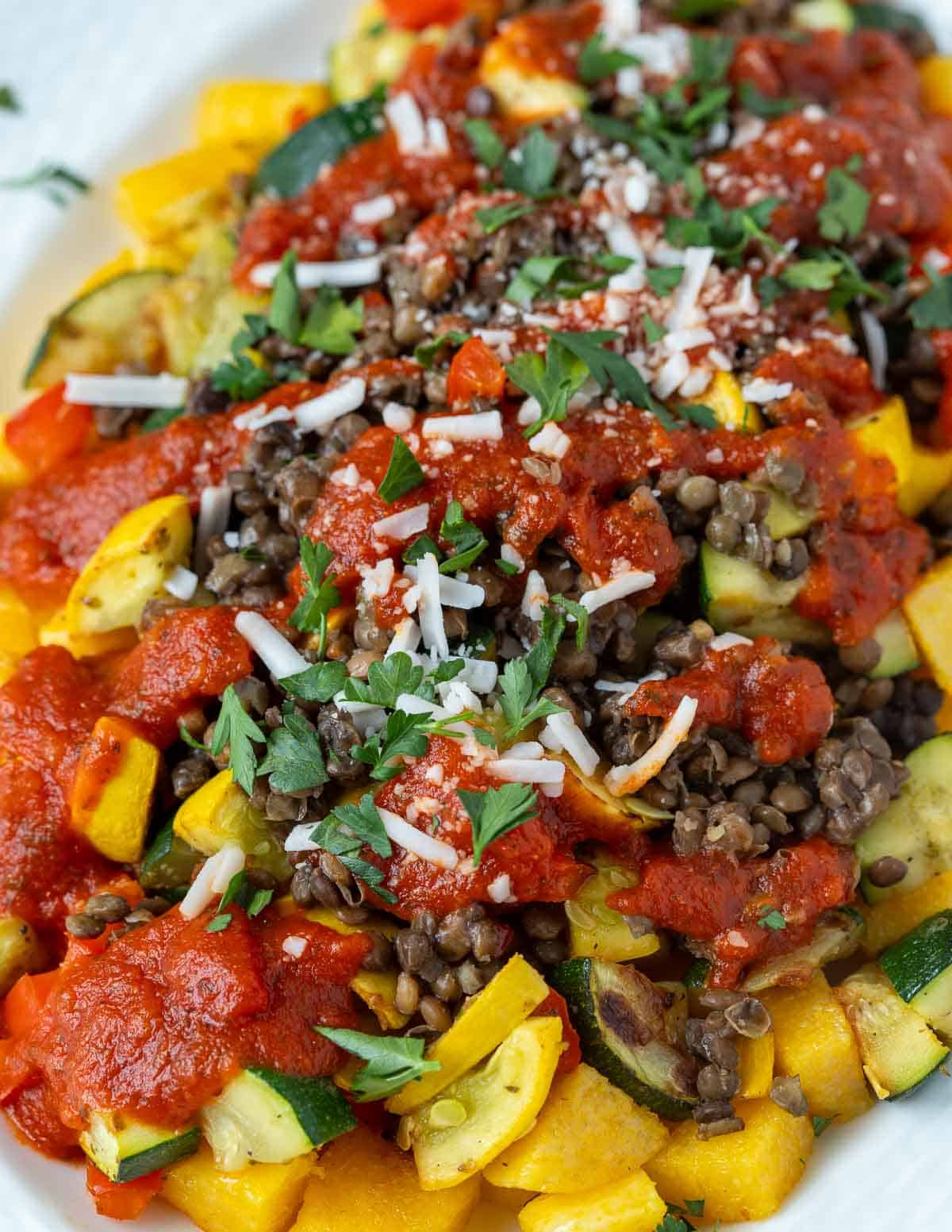 Baked polenta dish with roasted vegetables, lentils, marinara, vegan cheese, and parsley.