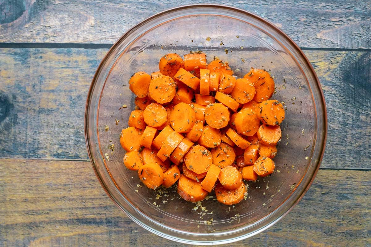 Chopped carrots in glass bowl with olive oil and herbs.