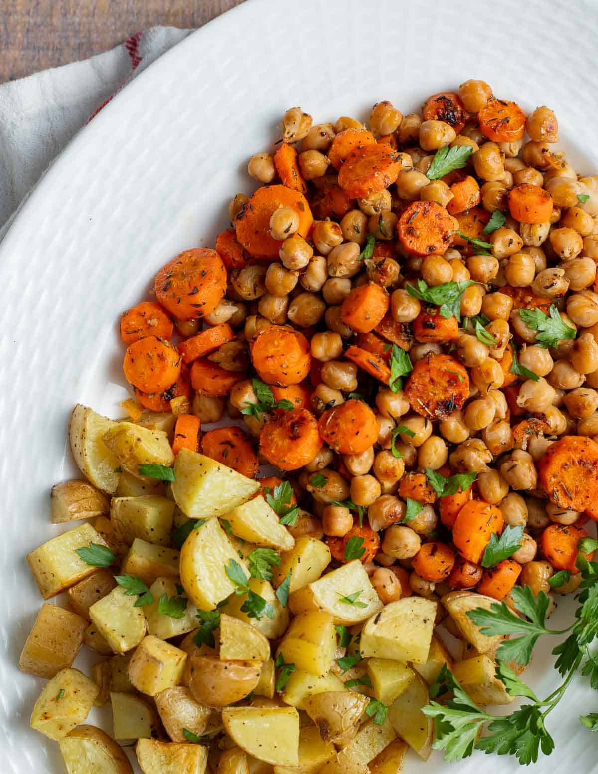Roasted potatoes, chickpeas, and carrots on a white serving platter.