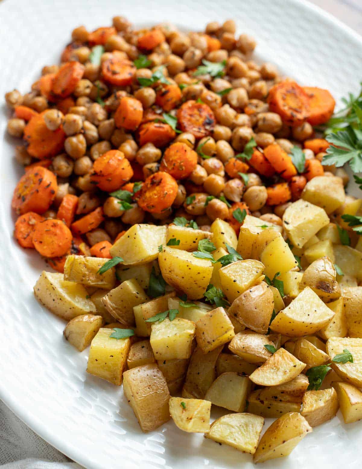 Roasted carrots, potatoes and chickpeas topped with fresh herbs on a serving platter.