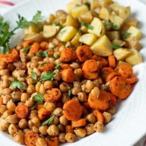 Roasted carrots, potatoes and chickpeas topped with fresh herbs on a serving platter.
