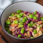Asian cabbage salad in a bowl topped with edamame.