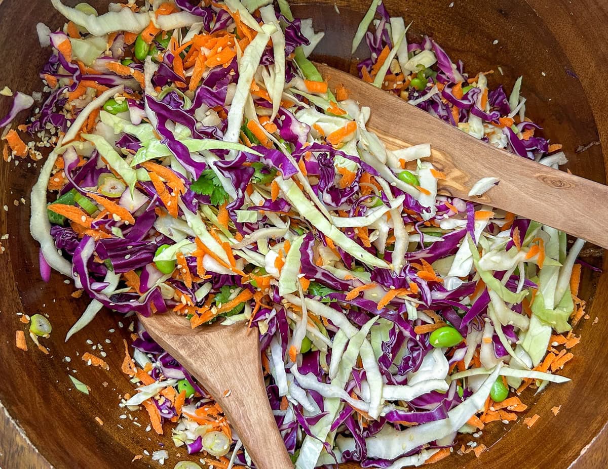 Asian cabbage salad tossed in peanut dressing in wood salad bowl.