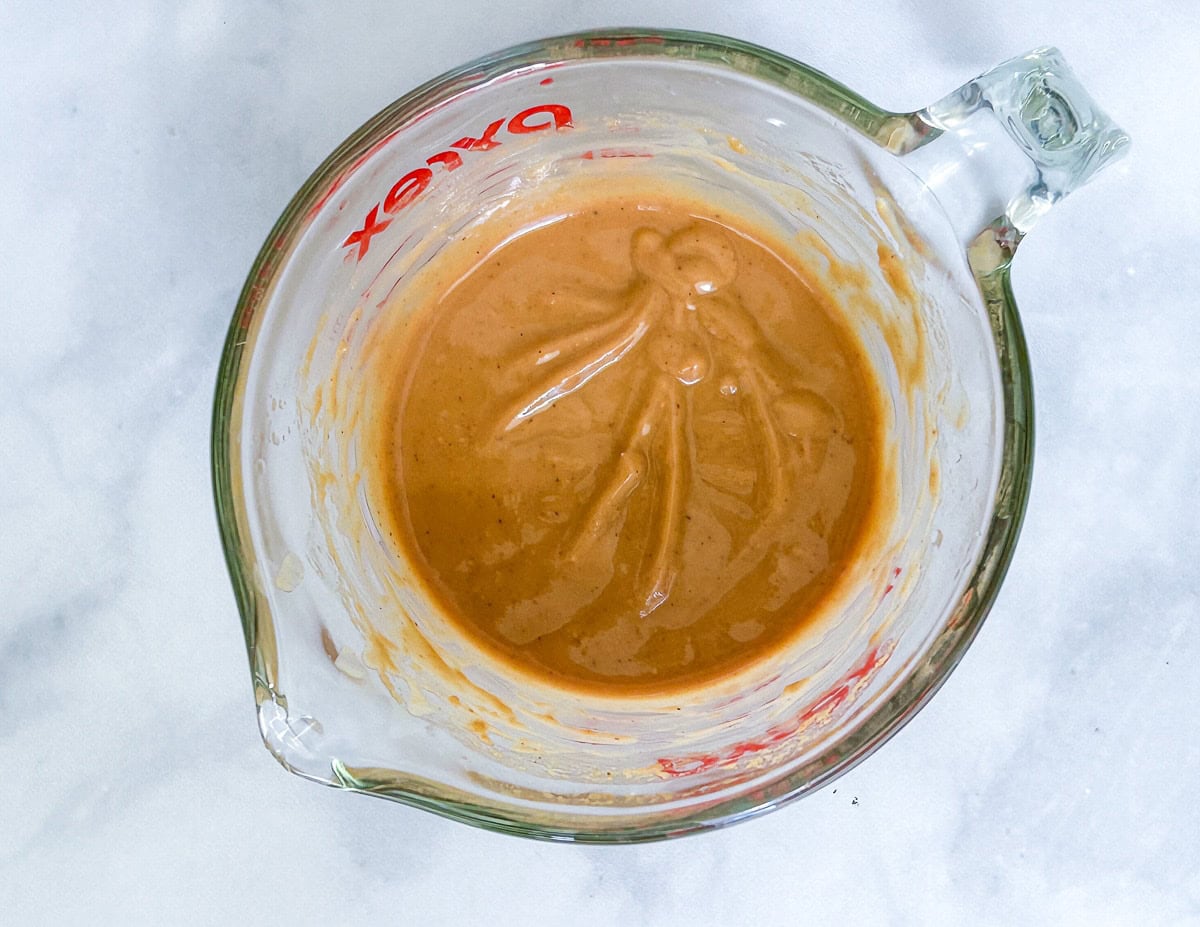 Peanut dressing in a glass measuring cup.